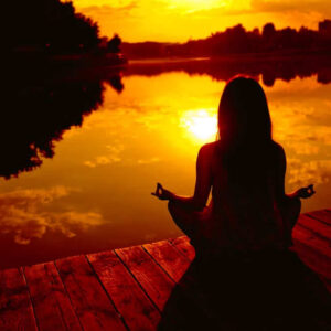 A Girl Is Sitting Near The Water In A Yoga Posture During Sunset